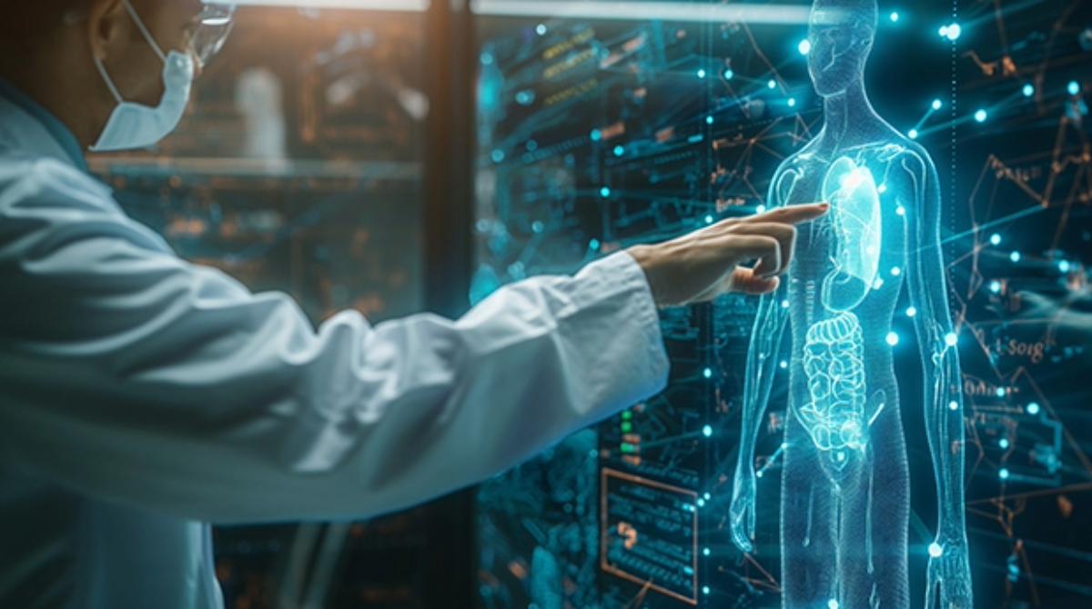 A scientist in a white coat and a blue surgical mask points at a futuristic computer image of a glowing abstract image of a human on a computer.