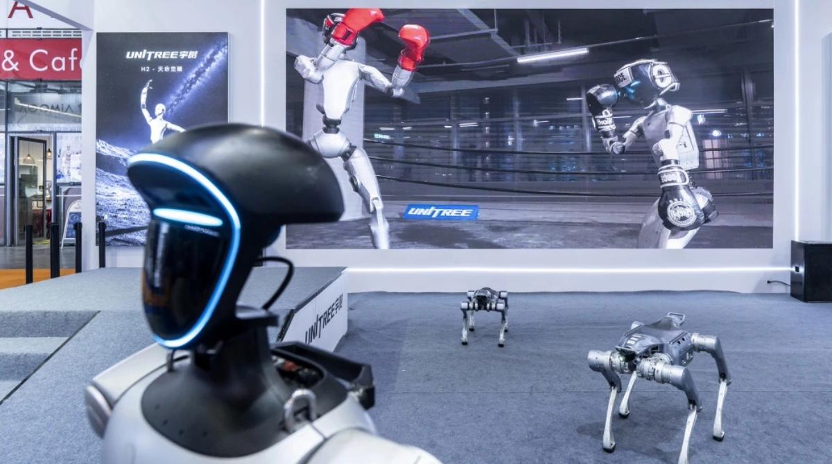 Two humanoid robots box as two doglike robots and a third humanoid robot approach the camera